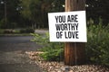 Closeup shot of You are worthy of love signage in front of a tree log near the road