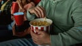 Closeup shot of young guy having popcorn basket while watching movie in cinema auditorium together with friends