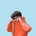 Closeup shot of a young male covering his face with an orange hoodie with glasses and neat hairstyle