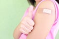 Closeup of shoulder of a vaccinated young Asian girl with adhesive bandage in thumbs up. Young people, children covid vaccination.