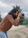 Closeup side view of a good looking young man with long hair and beard, taking photo in outdoor with DSLR Royalty Free Stock Photo