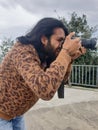 Closeup side view of a good looking young man with long hair and beard, taking photo in outdoor with DSLR Royalty Free Stock Photo