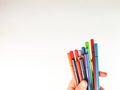 Closeup and side view of a hand holding many pens in different colors on white background as blank canvas for expressing