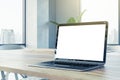 Closeup side view of a wooden office desk with white blank screen modern laptop, on city view window background in sunny interior Royalty Free Stock Photo