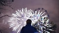 Closeup silhouette of man watching and photographing fireworks explode on smartphone camera outdoors