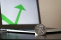 Closeup of silver coins with a green arrow on a laptop to show an increase in value