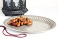 Closeup of silver plate with date fruits, prayer beads and ornamental dark Moroccan, Arabic lantern on the white table