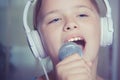 Closeup of singing caucasian child girl. Young girl emotionally sings into the microphone, holding it with hand.