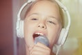 Closeup of singing caucasian child girl. Young girl emotionally sings into the microphone, holding it with hand.