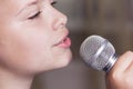 Closeup of singing caucasian child girl. Young girl emotionally sings into the microphone, holding it with hand. Royalty Free Stock Photo