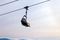 Snowboarder and skier in professional outfit climb up cable car lift up mountains on background of sky, sun and mountain peaks.