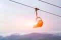 Snowboarder and skier in professional outfit climb up cable car lift up mountains on background of sky, sun and mountain peaks.