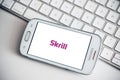 Closeup of Skrill logo on smartphone screen from Samsung brand on white keyboard background