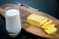 Closeup slice cheese on wooden board with fresh milk in the glass on black table background. Foods and drink concept. Dark tone