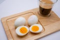 Closeup of sliced eggs and a glass of frothy black coffee on a wooden board, a healthy breakfast