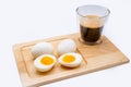 Closeup of sliced eggs and a glass of frothy black coffee on a wooden board, a healthy breakfast