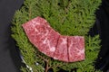 Closeup of slices of raw wagyu beef on evergreen leaves on a board