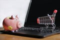 Closeup of a small shopping cart and a piggy bank on a laptop on the table - online shopping concept Royalty Free Stock Photo