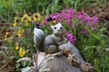 Closeup of a small squirrel statue on a rock in a garden covered in flowers