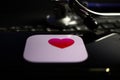 Closeup of smartphone screen with health app heart logo on computer keyboard, blurred stethoscope background