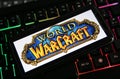 Closeup of smartphone screen with logo lettering of online game world of warcraft on illuminated computer keyboard