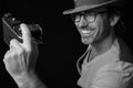 Closeup of a smiling man wearing fedora and glasses, taking a photo of himself using an old camera Royalty Free Stock Photo