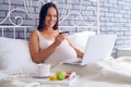 Smiling pregnant woman sitting on bed with laptop and credit car Royalty Free Stock Photo