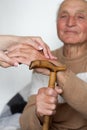 Closeup of smiling senior mans hands and young girl caregiver holding hands on walking stick Royalty Free Stock Photo