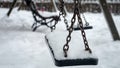 Closeup of snow slowly covering empty chain swings on winter children playground at park Royalty Free Stock Photo