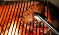 Closeup of someone turning a tasty steak cooking on a fire Royalty Free Stock Photo