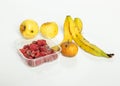 Closeup of spoilt raspberries in a plastic container, a banana peel and apples on a white background