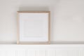 Closeup of square empty wooden picture frame on shelf. White beadboard wainscot wall paneling background. Scandinavian interior,