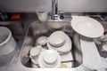 Closeup stack of dirty dishes at bottom of metal square sink at professional restaurant kitchen: white ceramic stack of plates, Royalty Free Stock Photo