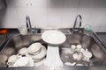 Closeup stack of dirty dishes at bottom of metal square sink at professional restaurant kitchen: white ceramic stack of plates, Royalty Free Stock Photo