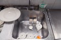 Closeup stack of dirty dishes at bottom of metal square sink at professional restaurant kitchen: white ceramic stack of plates, Royalty Free Stock Photo