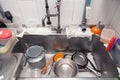 Closeup stack of dirty utensils in metal square sink at professional restaurant kitchen: stack of pans, colander, shovels faucet,