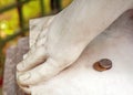 A stack of four Russian coins lying next to the feet of an antique marble statue with a blurred background