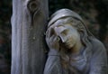 Of a statue of a female figure standing in a grassy area near a tree