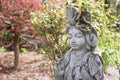 Closeup of a statue of Kwan Yin with red maple