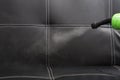 Closeup steam exiting nozzle of vapor cleaning machine, rinsing black leather couch