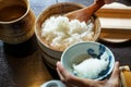 Closeup steamed japanese white rice in traditional wooden bowl with serving hands and wooden table background Royalty Free Stock Photo