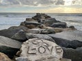 Closeup of a stone line carved the text "love", sea waves making foam,cloudy sky background