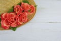 Closeup of a straw bonnet decorated with multiple silk roses on a white washed wooden background with copy space. Good for spring