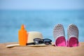 Closeup of straw hat, clogs shoes, sunscreen and black protective sunglasses on sandy beach at tropical seaside on warm sunny day Royalty Free Stock Photo