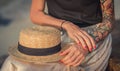 Closeup of a straw hat rests on his knees. Female hand with tattoos correct bracelets. The modern woman