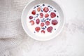 Closeup of strawberries and blueberries floating in milk in stoneware creamy bowl on clay textured background.