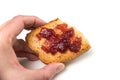Strawberry jam on cracker slice in hand on white background