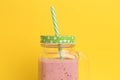 Closeup of a strawberry smoothie inside an aesthetically cute mason jar mug with green cap and straw