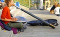 Closeup of street musician sitting on steps playing didgeridoo and hang handpan percussion instrument on sunny day