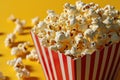 closeup striped paper box filled with tasty popcorn on a yellow background